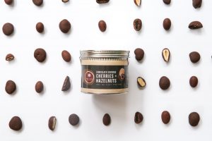 97078375_10158332746087258_3824205663081332736_o-300x200 A can of Askinosie chocolate-covered hazelnuts and cherries, surrounded by the chocolate pieces.
