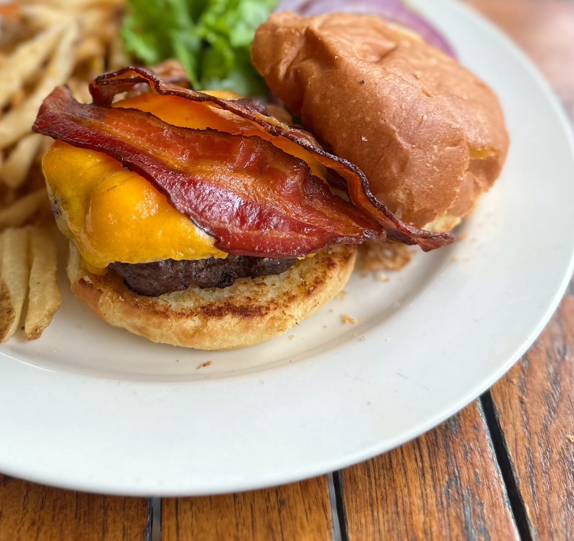 A burger with cheddar cheese an bacon on a plate with fries.