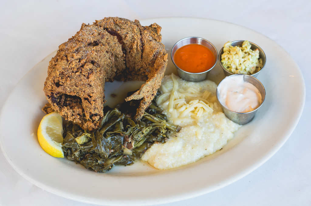 Golden fried whole catfish on a platter with collard greens and cheesy grits.