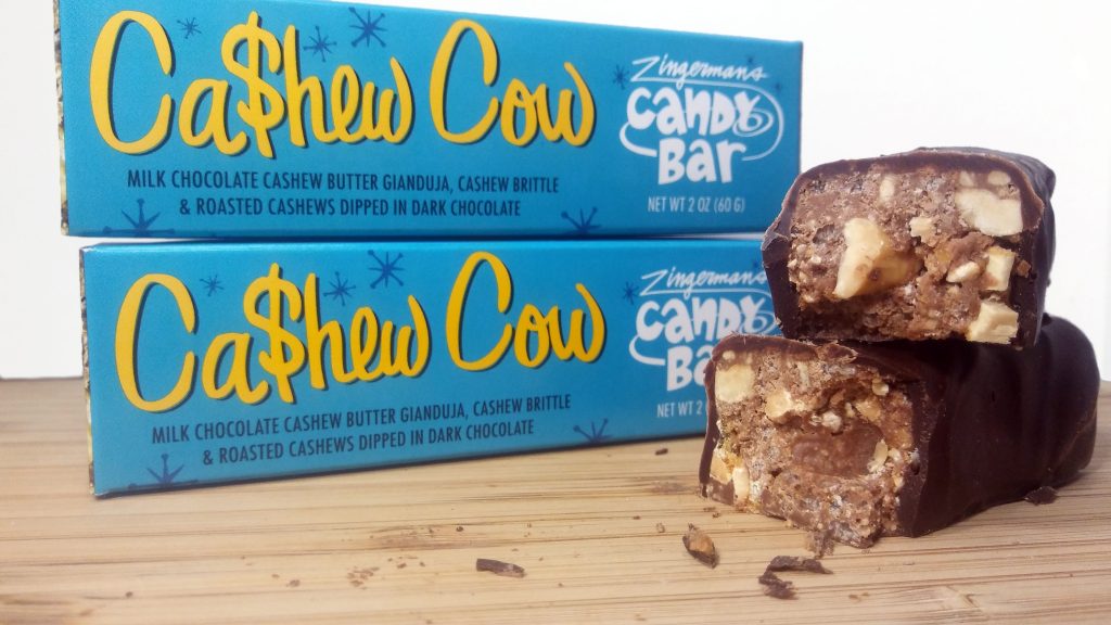 Two boxes of cashew candy bars from Zingermans's Candy sit next to two cut candy bars, revealing cashew and nougat wrapped in chocolate.