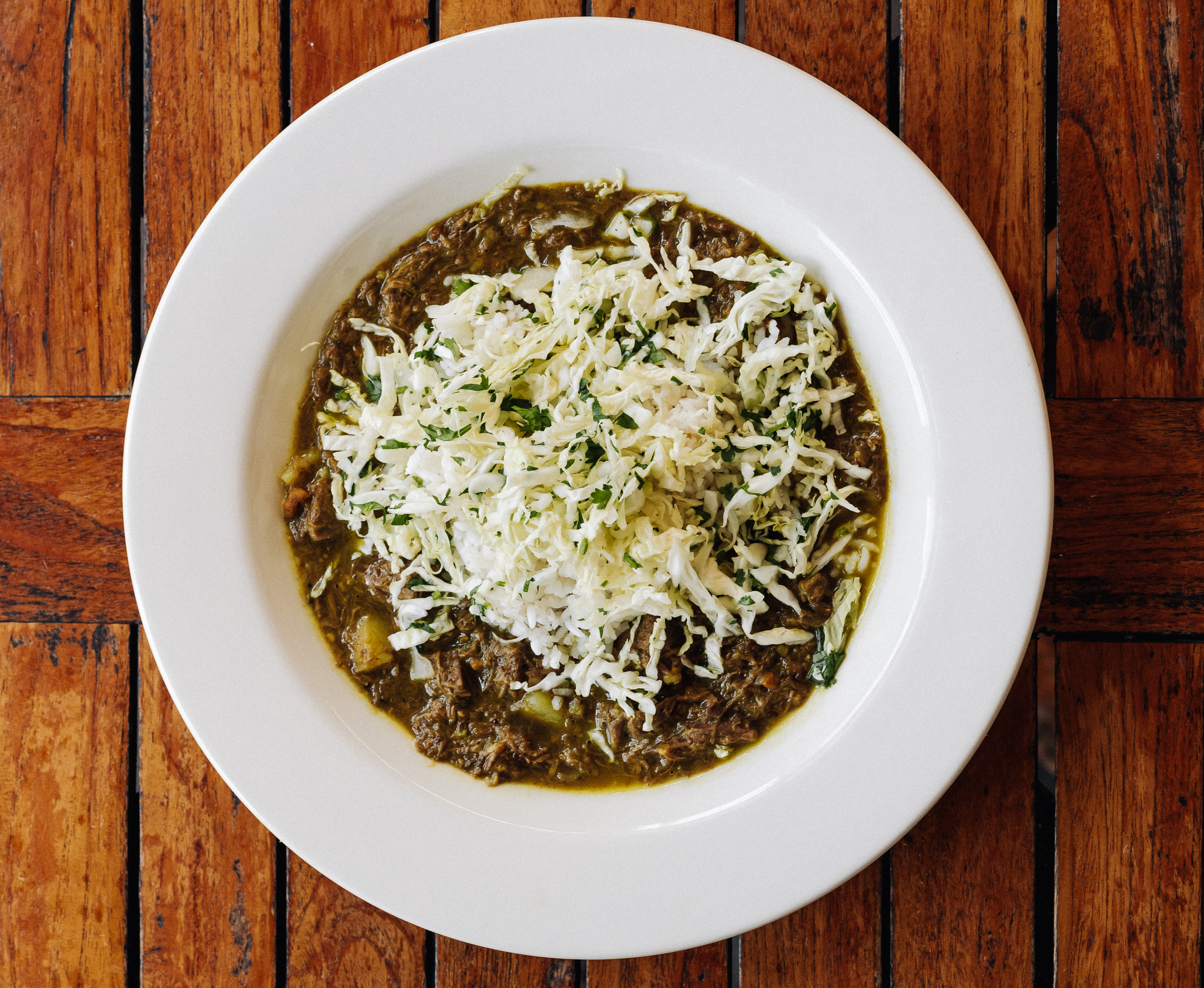 A large dish full of curried goat with a cabbage slaw on top.