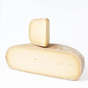 A half wheel of Pleasant Ridge Reserve cheese with a wedge sitting on top.