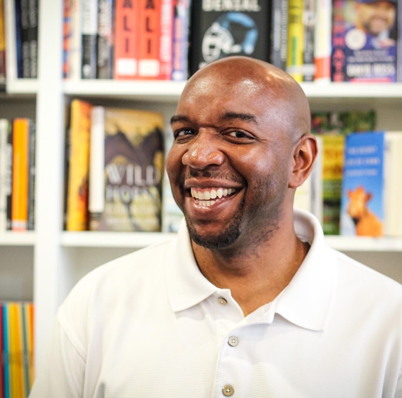Children's book author Malcolm Newsome smiles in front of a row of books
