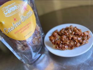 A bag of Zingeman's Candy manufactory Cashew Brittle sits next to a plate full of the brittle itself.