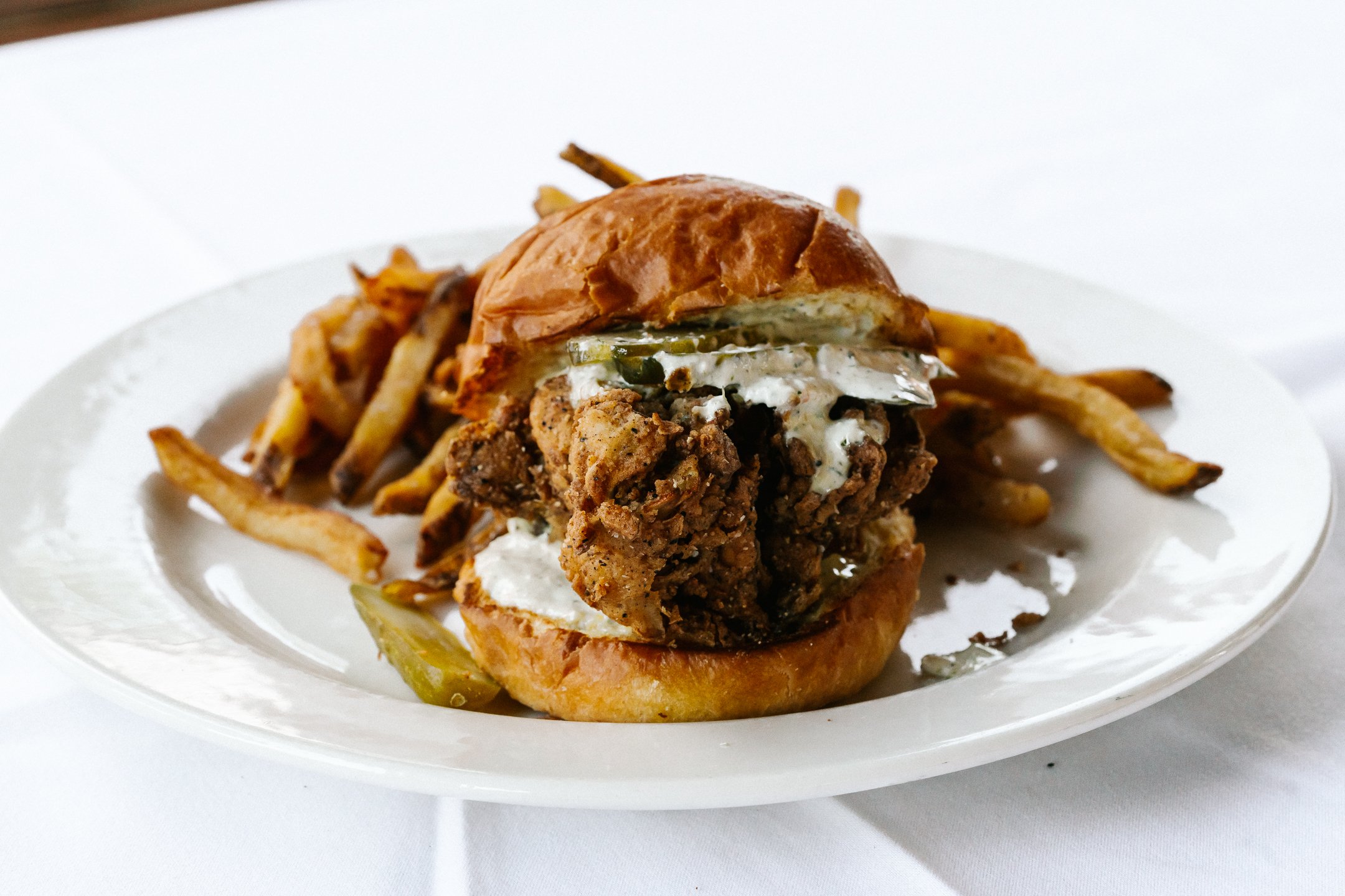 A golden fried chicken breast on a bun with ranch and sliced pickles
