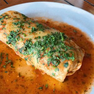 A burrito topped with fresh cilantro, and salsa ranchero