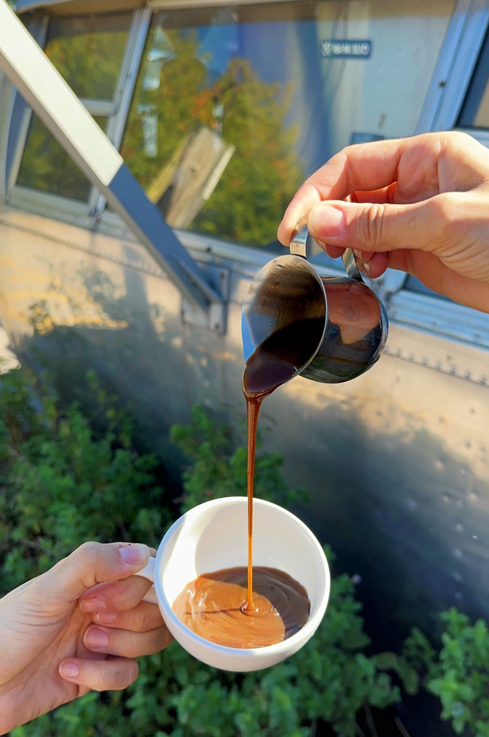 A hand pours a small pitcher of butterscotch syrup into a coffee cup