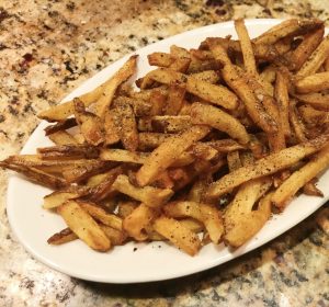 A plate full of golden fries dusted with black pepper.