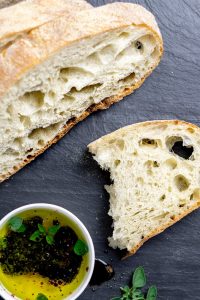 Slices of paesano bread next to a dish of olives and olive oil