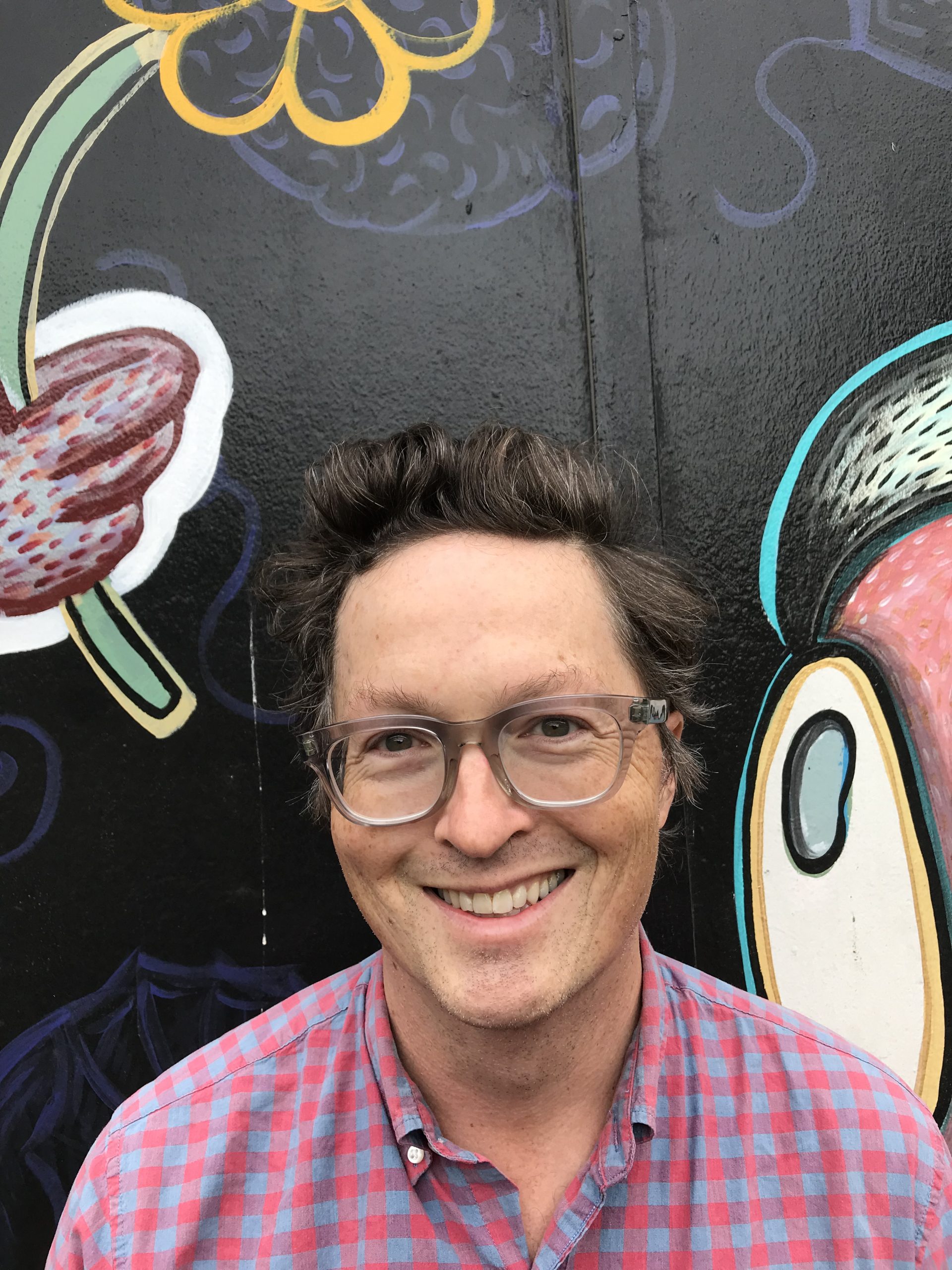 A photo of poet Michael Dickman, smiling in front of a colorful painting.