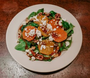 A spinach salad topped with sliced of bright California oranges and feta cheese crumbles