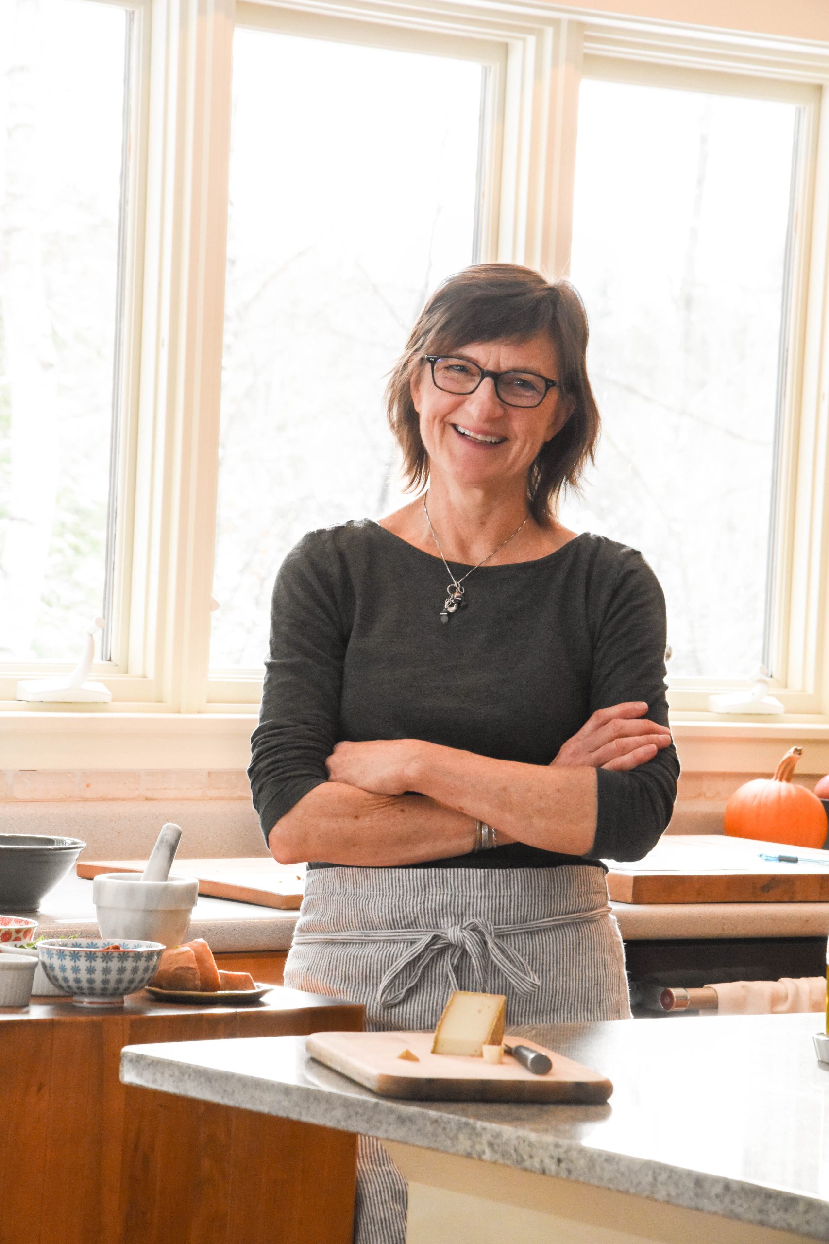 Chef Molly Stevens smiles in a kitchen with a plate of cheese and bread in front of her.