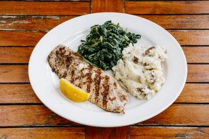 A plate of grilled fish, with a aside of mashed potatoes and spinach.