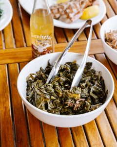 A bowl of collard greens with a pair of tings.