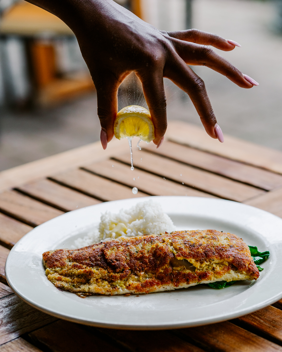 a plate of Herb crusted whitefish, with a hand squeezing a lemon on it