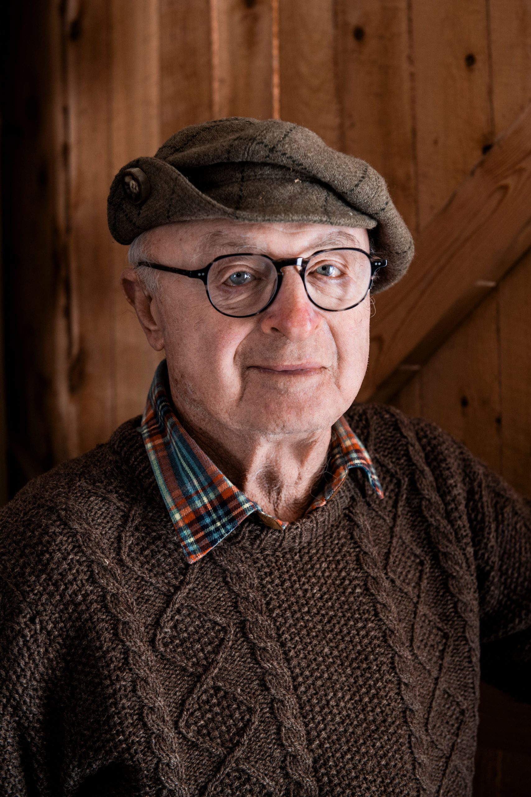 A photo of a gentleman wearing a brown sweater and a tweed cap, smiling