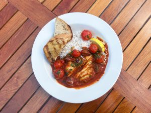A swordfish filet smothered in tomato sauce with bursting cherry tomatoes and white rice.