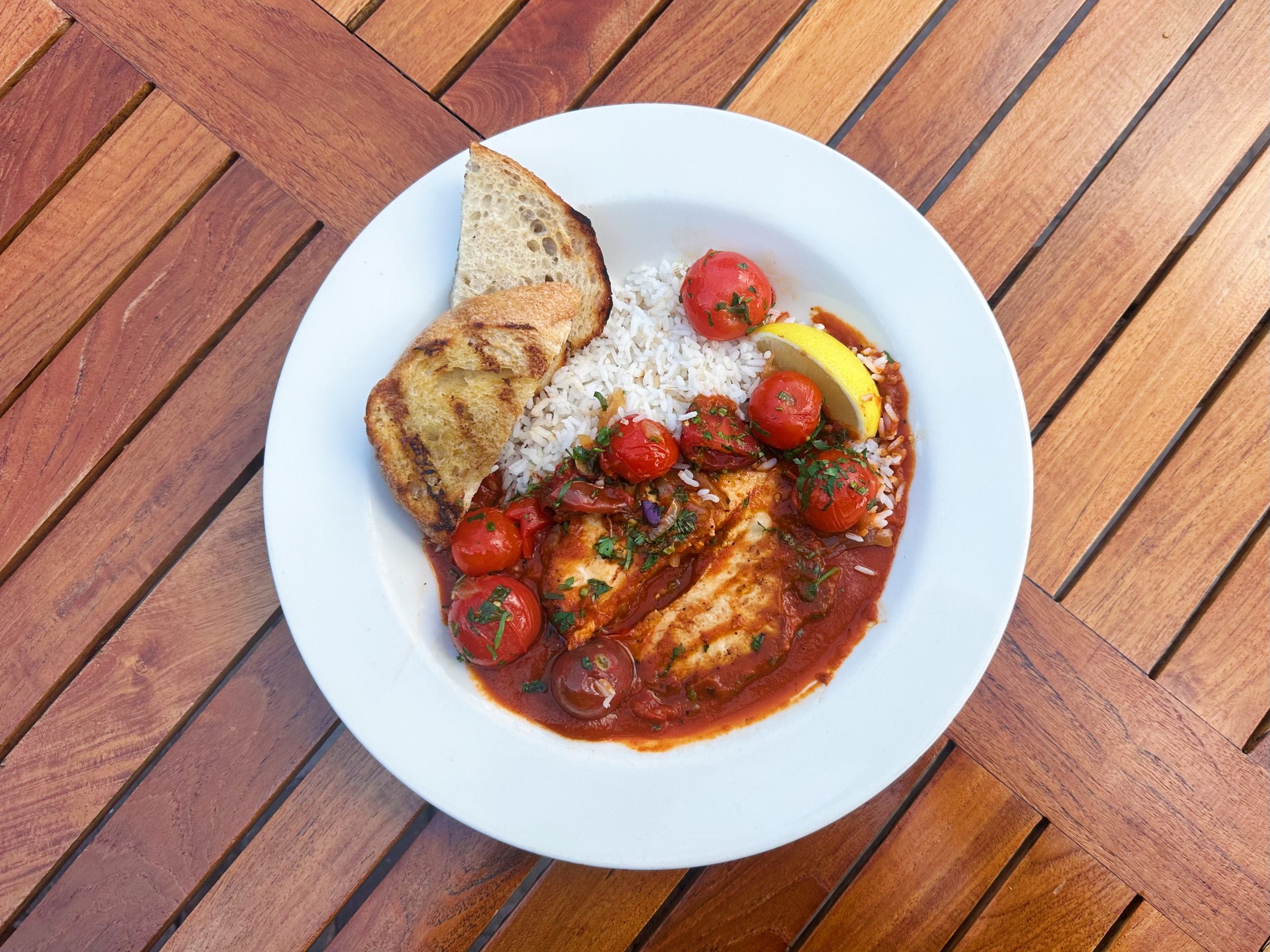 A swordfish filet smothered in tomato sauce with bursting cherry tomatoes and white rice.